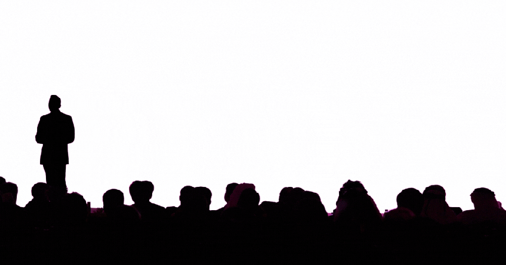 A presenter silhouetted against a pink screen reading Big Deck Energy in a packed auditorium